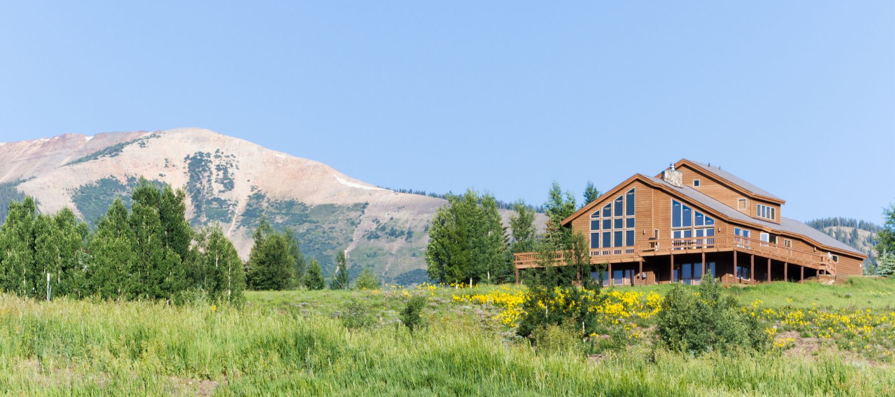 a home with wood exterior and large window wall in an open field with a mountain in the background