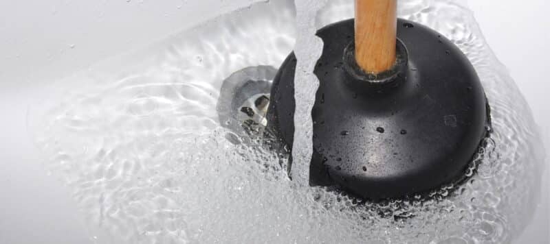 close up of a black plunger sitting in a sink full of water