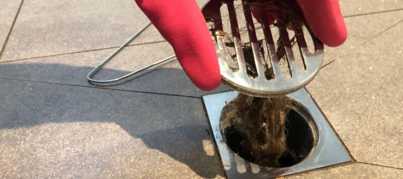 close up of a drain cover being removed by someone wearing red rubber gloves. a large amount of hair is connected to it