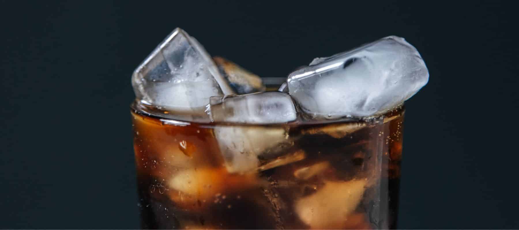 close up large ice cubes sticking out of a clear glass cup full of dark coke soda