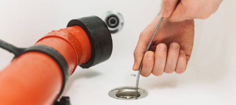 closeup of plumber unclogging a drain in a white sink